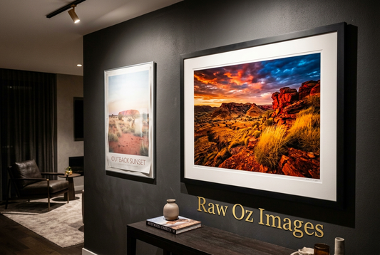 A faded outback poster beside a vivid framed fine art print of the same sunset scene on a dark wall.