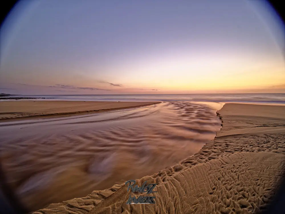 Fisheye view of pre-dawn light reflecting on glassy calm beach water